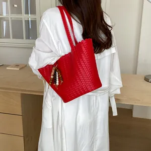 Detailed view of a red woven tote bag with a decorative beaded charm on a white shirt