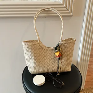 Vista detallada del bolso tote de paja crema para verano con un colgante floral.
