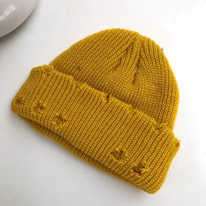 Close-up of a mustard yellow distressed knit beanie with ripped details for a street style look