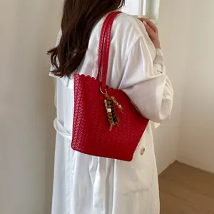 Detailed view of a vibrant red woven bucket tote bag worn by a model in a white trench coat