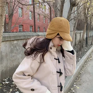 Side view of woman wearing warm camel earflap hat and beige winter coat outdoors.