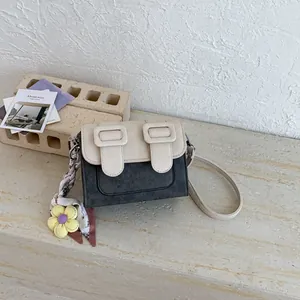 Close-up of two-tone square crossbody bag with decorative buckles and flower charm