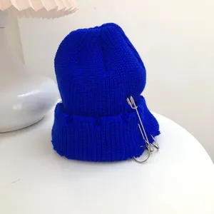 Detailed view of electric blue knit beanie with metal rings and pin decorations