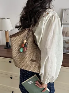 Handwoven straw tote bag with colorful bead charm for beach vacation or daily use.