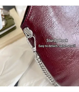 Close-up view of the sturdy silver metal hook and chain strap on a burgundy textured bag.