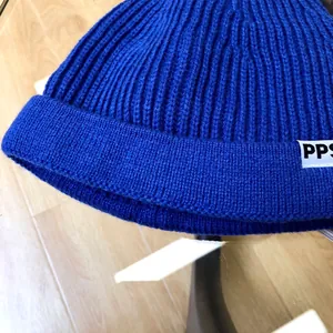 Detail of a bright blue children's ribbed knit beanie featuring a white PPS logo tag