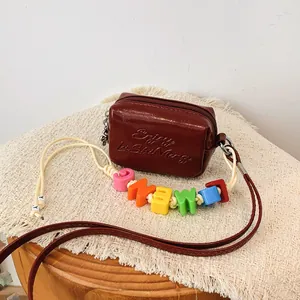 Detail of a burgundy mini crossbody bag with colorful alphabet bead decoration
