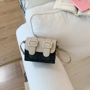 Detailed shot of a stylish color-block crossbody bag with rectangular buckles on a white sofa