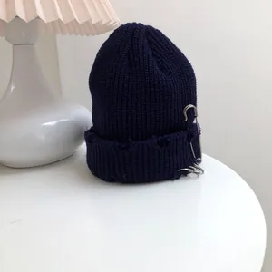 Close-up detail of navy blue distressed knit beanie with silver safety pin and rings
