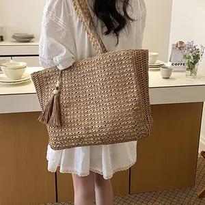 Détail d'un grand sac cabas en paille tissée avec un pompon décoratif porté par un mannequin.