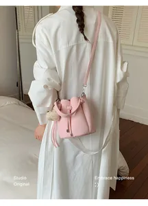 Close-up of pink pebbled leather bucket bag with drawstring and plush charm.