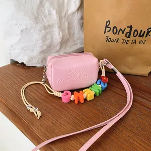 Close-up of pink mini crossbody bag with colorful letter beads and embossed text detail.