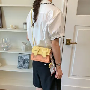 Small crossbody square bag in yellow and orange color-block design worn on shoulder