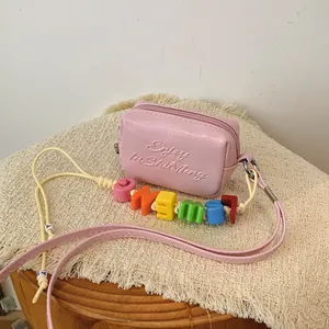 Detail of a pink mini crossbody bag with colorful alphabet beads on a yellow cord.
