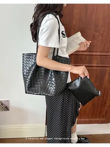 Macro view of a stylish black woven leather tote bag carried by a fashion model.