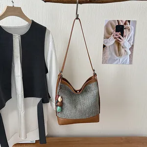 Detail of a woven bucket bag with brown leather trim and a colorful beaded charm accessory.