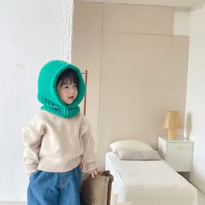 Child wearing a green knitted balaclava hood in a cozy bedroom setting