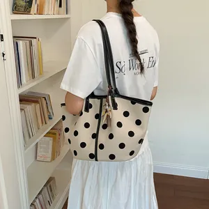 Elegant cream and black polka dot shoulder tote bag carried by model in a library.