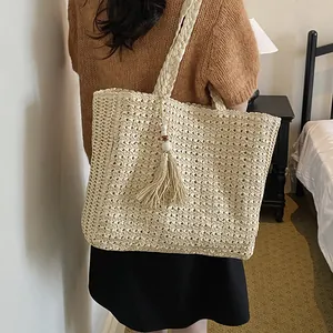 Détail d'un sac cabas tissé minimaliste avec pompon décoratif porté par une femme élégante