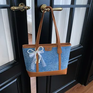 Sac cabas en denim bleu avec garniture marron sur une poignée de porte et nœud en dentelle.