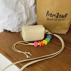 Close-up of a cream mini crossbody bag with colorful alphabet bead strap and embossed text.