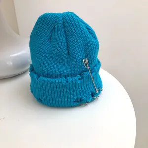 Detail of blue distressed knitted beanie with metal ring and safety pin accessories.