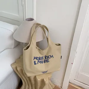 Vista detallada de bolsa tote de lona beige con texto bordado azul MORE RICH & MORE elegante