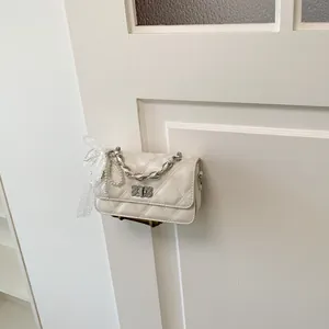 White quilted small square crossbody bag with pearl and lace bow charm hanging on a door