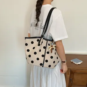 Modern cream polka dot tote bag with a palm tree charm carried by a woman in a white outfit