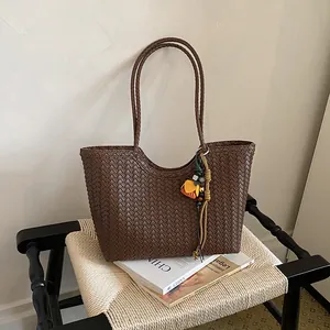 Vista detallada de bolso tote tejido marrón con colgante floral sobre una silla
