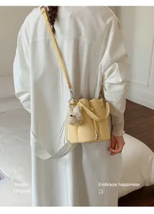 Stylish yellow bucket bag with a cute plush bear charm detail over a white coat