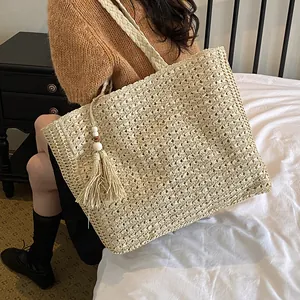 Détail montrant un grand sac cabas en paille tissée avec un pompon sur un lit blanc.