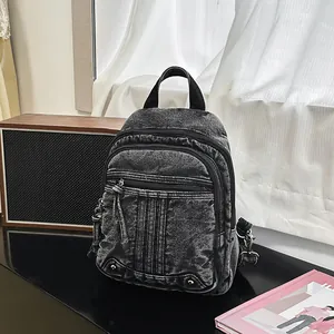 Close-up of a stylish black denim backpack with multiple zipper pockets on a vintage desk