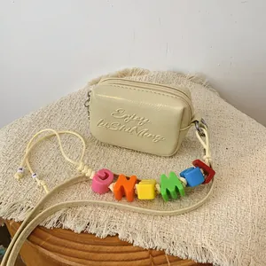 Minimalist cream mini crossbody square bag featuring a colorful alphabet bead strap detail