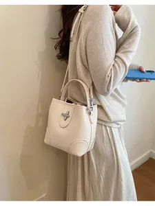 Sac seau rétro en cuir grainé crème avec fermoir rotatif argenté porté par un mannequin