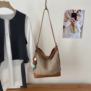 Stylish woven straw bucket bag with brown leather trim and beads hanging on a white wall