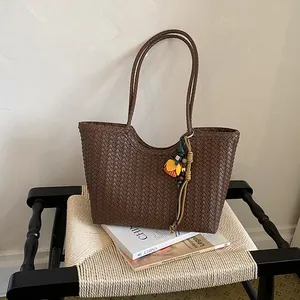 Vista detallada de un bolso tote trenzado marrón con colgante floral sobre una silla