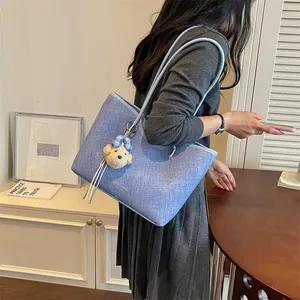Detailed shot of a large light blue textured tote bag with a cute teddy bear charm