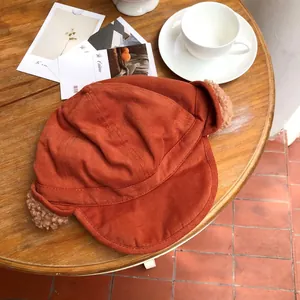 Cozy burnt orange trapper hat with soft faux fur ear flaps on a wooden table.