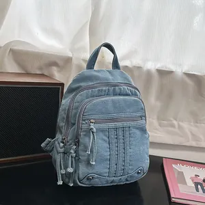 Close-up of blue denim backpack featuring multiple tassel zippers and stitched details