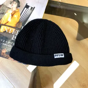 Detailed view of a black children's knitted beanie hat with a white PPSW tag on a magazine.