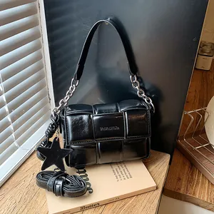 Detail view of a black woven underarm bag with silver chain strap and star charm