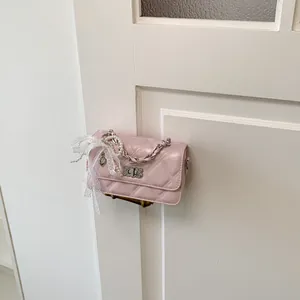 Detailed view of a pink quilted crossbody bag with pearl and lace charm decoration