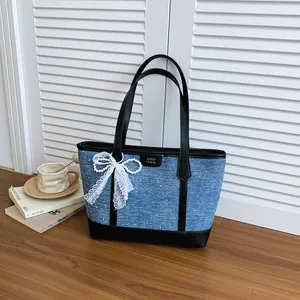 Détail du sac fourre-tout en denim bleu avec garniture noire et nœud en dentelle blanche