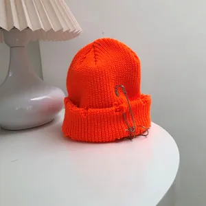 Detail of a neon orange knit beanie with safety pin rings and distressed edges