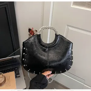 Detailed view of a stylish black patent leather handbag featuring a silver metal handle and studs