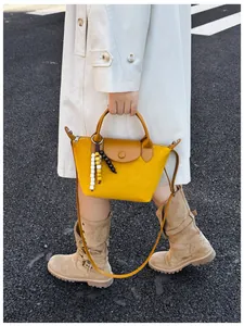 Vue détaillée d'un sac dumpling jaune vif en daim avec poignées en cuir et charms