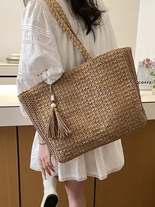 Grand sac cabas en paille tissée à la mode avec pompon porté par un beau mannequin