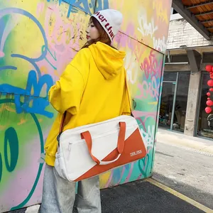 Fashionable white and orange sports duffel bag carried by a model against a graffiti wall.