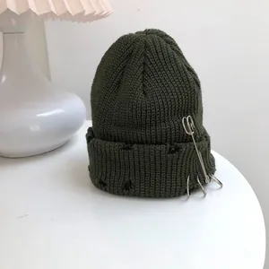Distressed olive green knit beanie featuring silver rings and safety pin detail